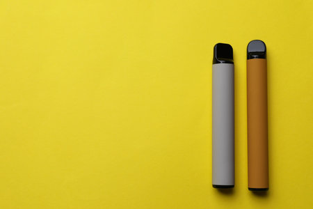 Different electronic cigarettes on yellow background, flat lay. Space for textの写真素材