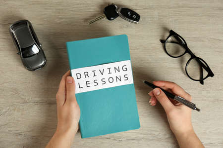 Woman with workbook for driving lessons and car key at wooden table, top view. Passing license examの写真素材