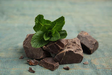 Tasty dark chocolate pieces with mint on blue wooden table