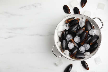 Colander with raw mussels and ice on white marble table, flat lay. Space for textの写真素材