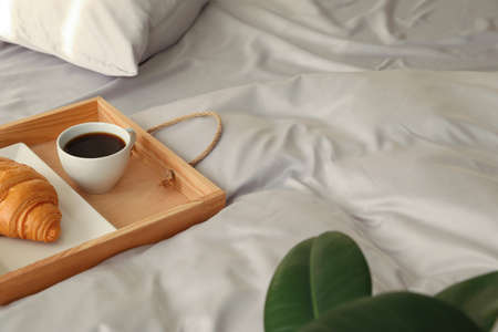 Tasty croissant and aromatic coffee on bed with stylish silky lines, space for textの写真素材