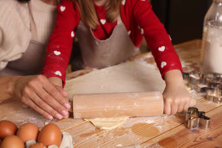 Mother and her daughter making delicious Christmas cookies at wooden table, closeup