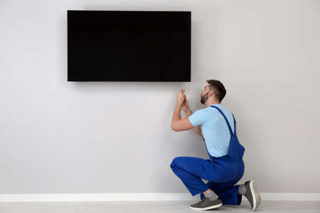 Professional technician with screwdriver installing modern flat screen TV on wall indoors