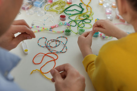 Father with his daughter making beaded jewelry at table, closeup