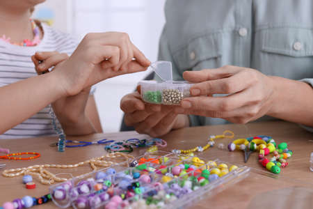 Mother with her daughter making beaded jewelry at home, closeupの写真素材