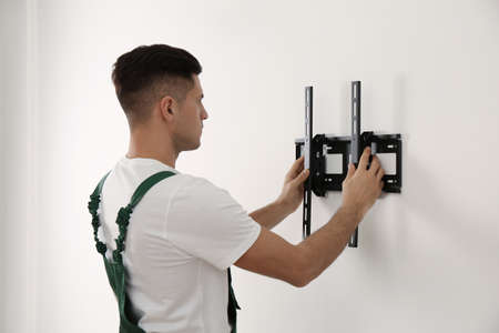 Professional technician installing TV bracket on wall indoors