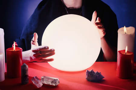 Soothsayer using glowing crystal ball to predict future at table in darkness, closeup. Fortune...