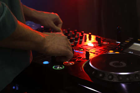 DJ creating music on modern console mixer in night club, closeup