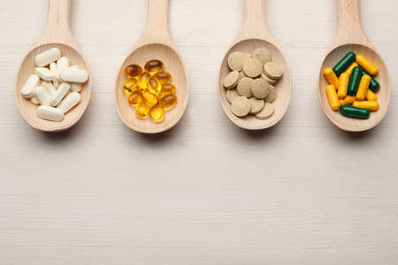 Spoons with different dietary supplements on white wooden table, flat lay. Space for text