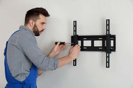 Professional technician with screwdriver installing TV bracket on wall indoorsの写真素材