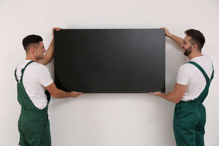 Professional technicians installing modern flat screen TV on wall indoors