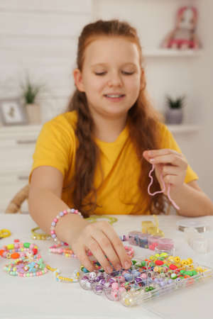 Cute girl making beaded jewelry at table in room, focus on handの写真素材