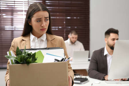 Upset dismissed woman carrying box with personal stuff in officeの写真素材