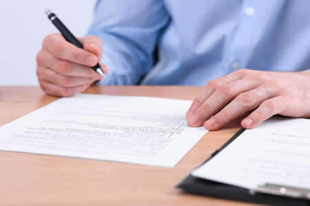 Businessman signing contract at wooden table, closeup of hands
