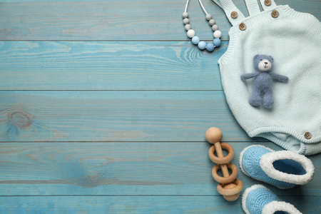 Cute knitted baby bodysuit, booties and toys on light blue wooden background, flat lay. Space for textの写真素材