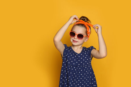 Cute little girl wearing stylish bandana and sunglasses on orange background, space for textの写真素材