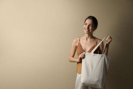 Happy young woman with blank eco friendly bag against beige background. Space for textの写真素材