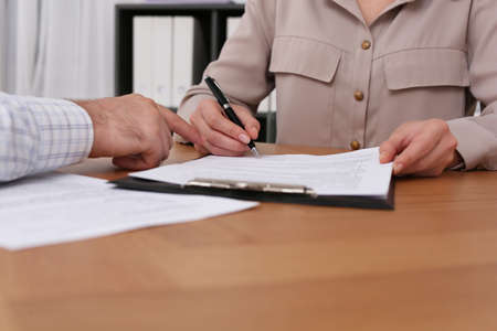 Businesspeople signing contract at wooden table indoors, closeup of handsの写真素材
