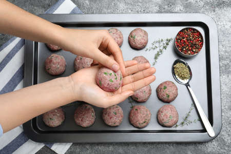 Woman making fresh raw meatballs at gray table, top view