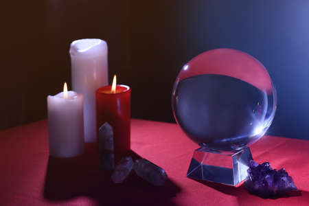 Crystal prediction ball, candles and stones on table in darkness. Fortune telling