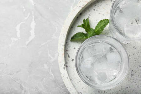 Glasses of soda water with ice and mint on gray table, top view. Space for text