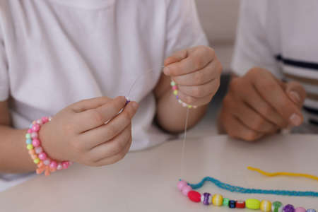 Father with his daughter making beaded jewelry at table, closeup