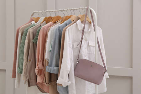 Rack with stylish women's clothes near light wall
