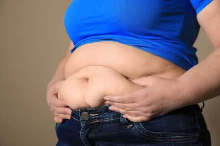 Overweight woman in tight shirt and jeans on light brown background, closeupの写真素材