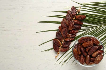 Tasty sweet dried dates and palm leaf on white wooden table, flat lay. Space for textの写真素材