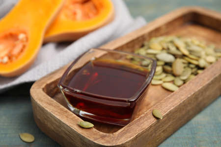 Glass bowl of oil and pumpkin seeds on wooden table, closeup