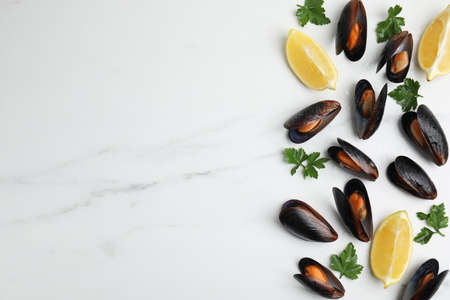 Cooked mussels with parsley and lemon on white marble table, flat lay. Space for textの写真素材