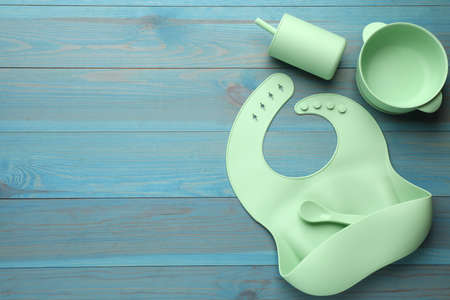 Flat lay composition with silicone baby bib and plastic dishware on light blue wooden background. Space for textの写真素材