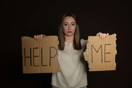 Unhappy young woman with HELP ME sign on dark backgroundの写真素材