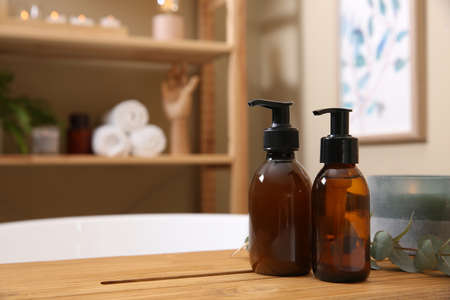Dispensers of liquid soap, burning candle and eucalyptus branch on bath tray indoors. Space for textの写真素材