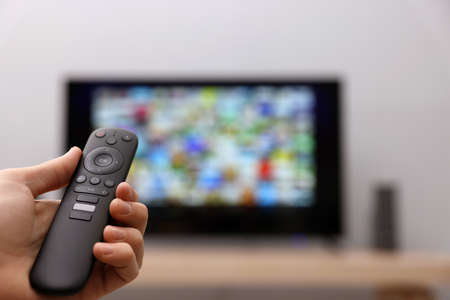 Woman switching channels on TV set with remote control at home, closeup. Space for textの写真素材