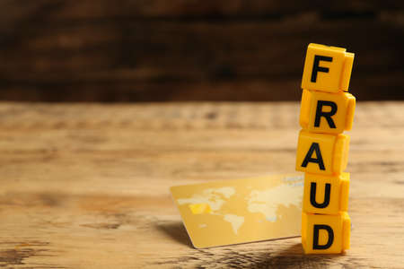 Word Fraud of yellow cubes with letters and credit card on wooden background. Space for text