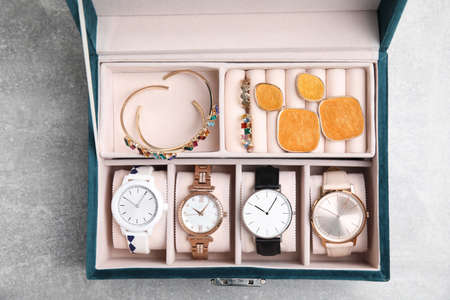 Elegant jewelry box with beautiful bijouterie and expensive wristwatches on light gray stone table,...