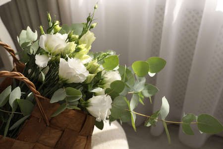 Stylish wicker basket with bouquet of flowers in room, closeupの写真素材