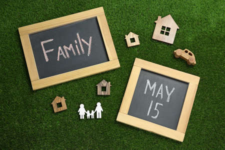 Chalkboards and wooden figures on green grass, flat lay. International Family Day