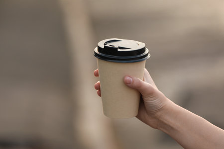 Woman holding paper coffee cup on blurred background, closeupの写真素材