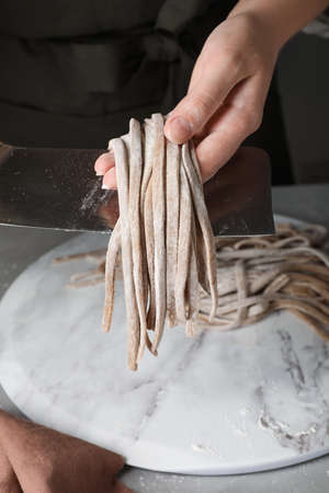 Woman making soba (buckwheat noodles) at gray table, closeup