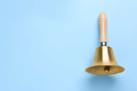 Golden school bell with wooden handle on light blue background, top view. Space for text