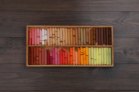 Drawing pastel set in box on wooden background, top view