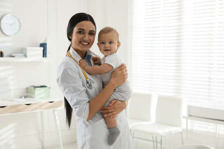 Young pediatrician with cute little baby in clinic. Space for text