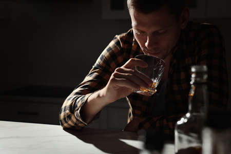 Addicted man drinking alcohol at table in kitchenの写真素材