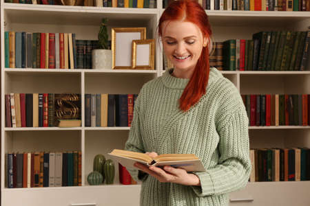 Beautiful young woman reading book in room. home library