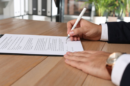 Businessman signing contract at wooden table indoors, closeup