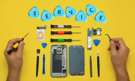 Man repairing broken smartphone on yellow background, top viewの写真素材