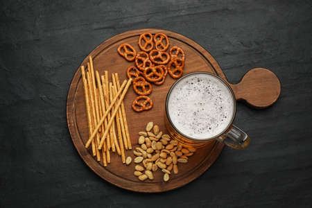 Glass of beer served with delicious pretzel crackers and other snacks on black table, top viewの写真素材