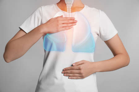 Woman holding hands near chest with illustration of lungs on light gray background, closeup